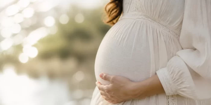 Kas vyksta nėštumo pradžioje: besilaukianti moteris laiko ranką ant pilvo, simbolizuojanti ankstyvojo nėštumo pradžią